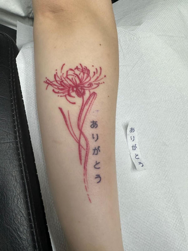 Hình xăm hoa bỉ ngạn kết hợp với dòng chữ Nhật"ありがとう" (Arigato), có nghĩa là "cảm ơn". Hoa bỉ ngạn gắn liền với sự chia ly trong văn hóa Nhật Bản cùng chữ cảm ơn tượng trưng cho lòng biết ơn với con người hoặc trân trọng kỷ niệm đã qua
