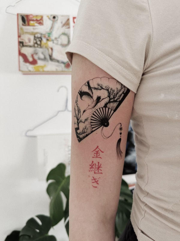 Sự kết hợp giữa hình xăm quạt và chữ "金継ぎ" (Kintsugi) tượng trưng cho việc tìm thấy vẻ đẹp và sự bình yên trong những trải nghiệm cuộc sống, chấp nhận những khuyết điểm và biến chúng thành nguồn sức mạnh độc đáo